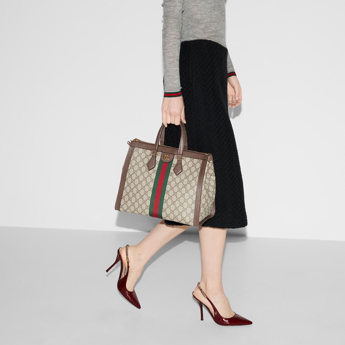 Beige-and-brown GG-pattern tote with green-red-green stripe, carried by a model